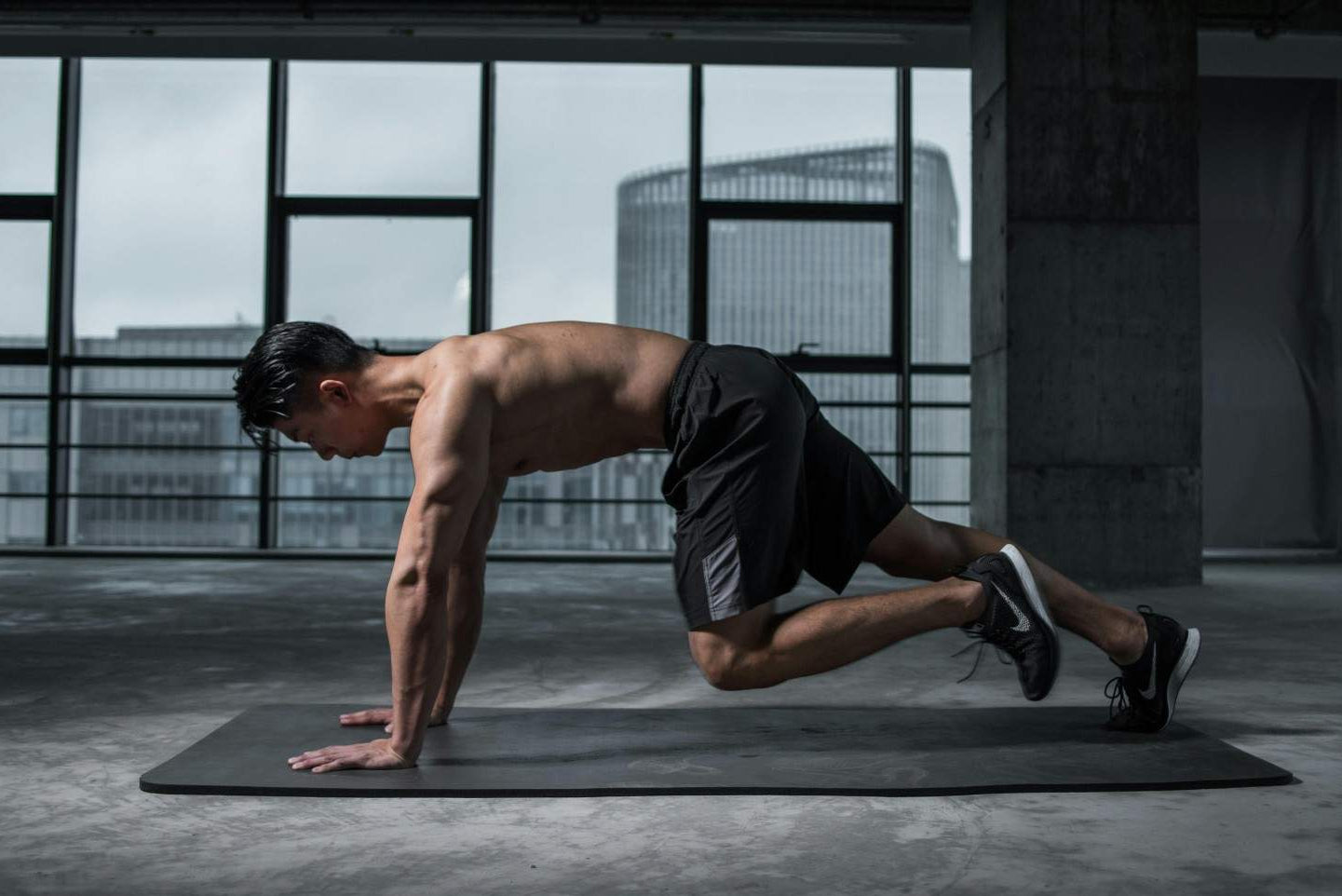 Man performing a yoga pose in a modern indoor setting with large windows.